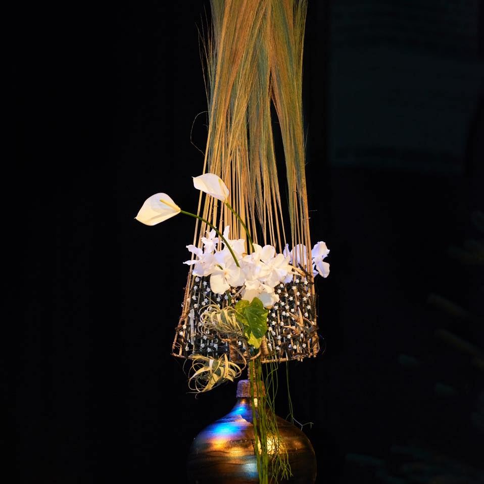 Florale Installation mit Calla und Orchideen vor dunklem Hintergrund